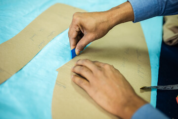 Young African American tailor drawing with chalk on material in his own atelier.