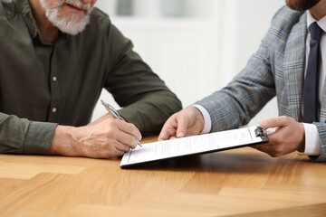Notary showing senior man where to sign Last Will and Testament at wooden table indoors, closeup
