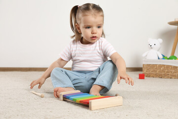Cute little girl with xylophone and drumsticks at home