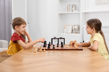 Cute children playing chess at table in room