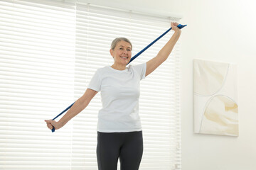 Fototapeta na wymiar Senior woman doing exercise with fitness elastic band at home