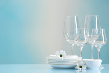 Set of many clean dishware, flowers and glasses on light blue table. Space for text
