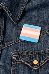 large square pin with the trans flag on a denim shirt