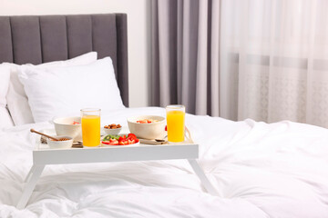 Fototapeta na wymiar Tasty breakfast served in bed. Oatmeal, juice, fruits, almonds and honey on tray, space for text