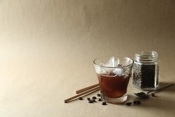 Refreshing iced coffee in glass, beans and straws on beige background. Space for text