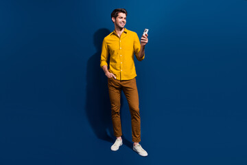 Full size photo of attractive young man hold device read post news dressed stylish yellow clothes isolated on dark blue color background