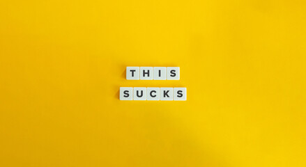 This Sucks Slang Term. Text on Block Letter Tiles on Yellow Background.
