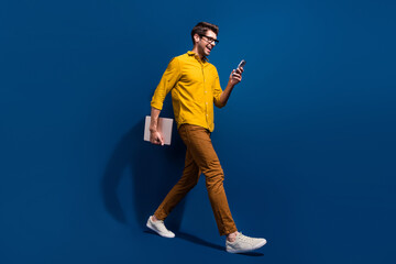 Full length photo of nice young male walk netbook hold gadget excited wear trendy yellow garment isolated on dark blue color background
