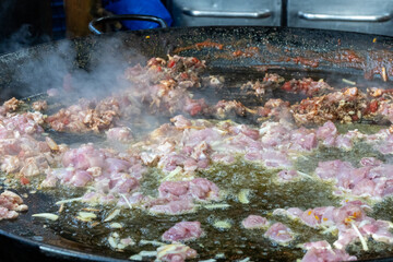 Sea food is cooking in a large pan at a market stall. Steam is rising as it cooks.
