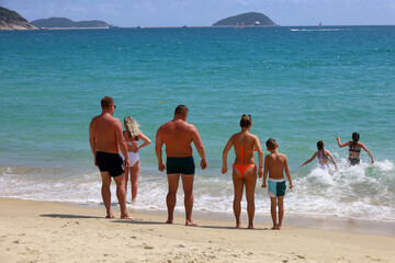 Two families with children tanning on a sandy sea beach. Kids going to swim in azure water