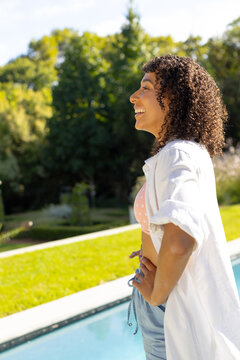 Young biracial woman enjoys the sunshine near a pool, she exudes happiness and relaxation in a seren