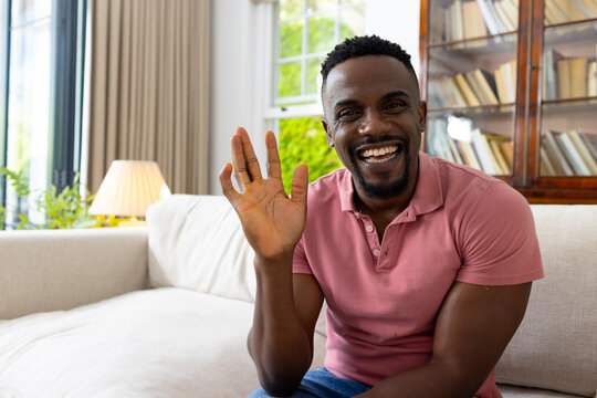 African American man in a pink polo shirt waves with a bright smile on a video call