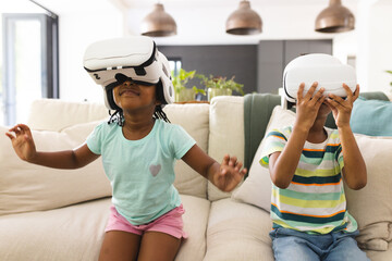 African American sister and brother are immersed in virtual reality, sitting on a couch