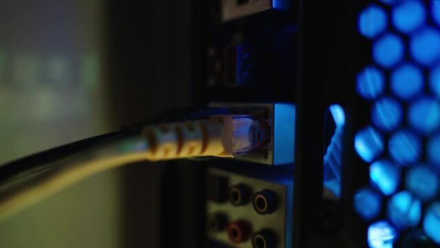 A woman's hand plugs in a wired internet cable into the Ethernet port of the PC, and the data transfer lights start blinking. Dolly slider, close up.