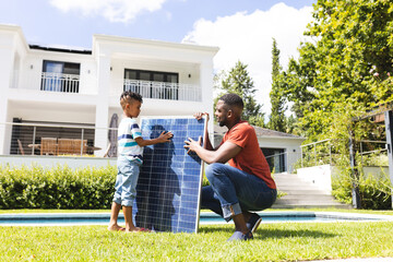 African American father and son examine a solar panel outdoors