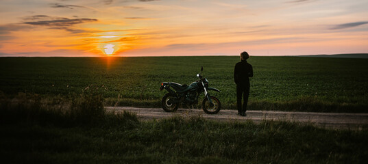motorcyclist on an enduro motard motorcycle in a field at sunset