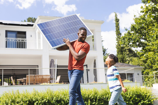 African American father carries a solar panel while a son walks beside him