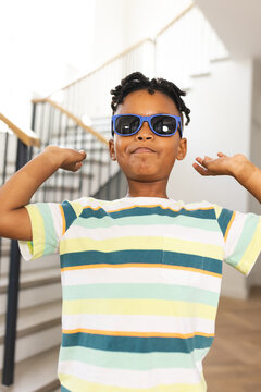 African American boy flexes his muscles, wearing sunglasses and a striped shirt