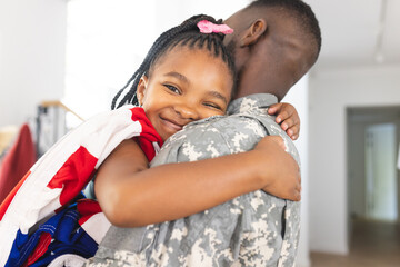 African American girl embraces a soldier, her smile radiates joy, with an American flag