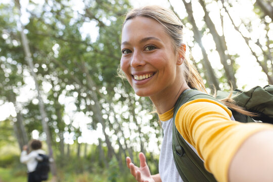 Young Caucasian woman smiles at the camera, extending her hand for a selfie with copy space on a hik