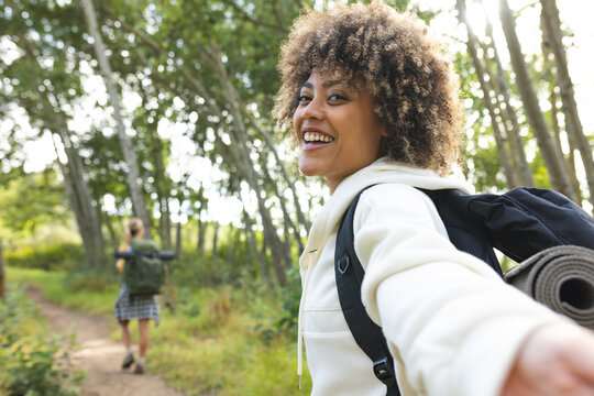 Young biracial woman with curly hair smiles while hiking, leading the way on a forest trail hike wit
