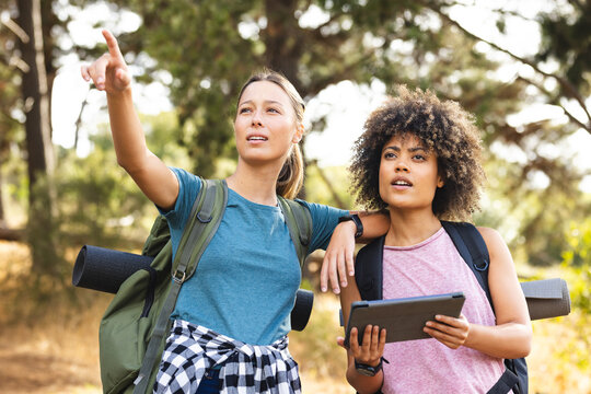 Young caucasian woman points out direction while hiking with biracial woman holding  tablet
