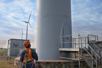 maintenance engineer standing  against turbines on wind turbine farm.