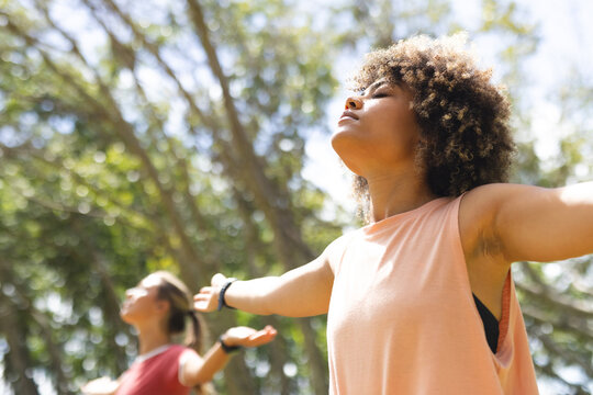 Young biracial woman with curly hair enjoys a moment of relaxation outdoors, arms outstretched, with