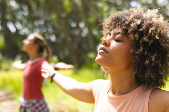 Young biracial woman with curly hair enjoys a moment of relaxation outdoors, eyes closed and arms ou