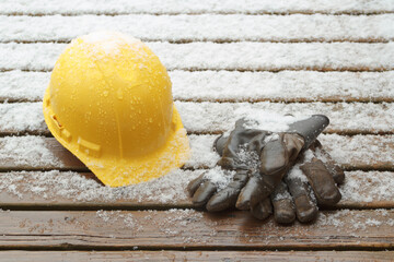 Hard hat and work gloves on wet deck boards with light snow