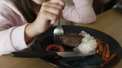 Obraz na płótnie Canvas Little girl eating lunch, 8 year old child enjoying mealtime food. Plate of meat, veggies and rice
