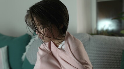 Little girl putting sweater and adjusting hair seated on couch in the evening. Child getting ready, putting clothes on after bathtime