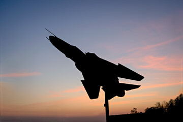 Sun rises behind silhouette image of Indian Air Force's fighter jet plane MIG-29 displayed at NDA chowk in Pune. - obrazy, fototapety, plakaty