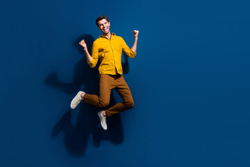 Fototapeta na wymiar Full size photo of attractive young man jump raise fists celebrate wear trendy yellow clothes isolated on dark blue color background