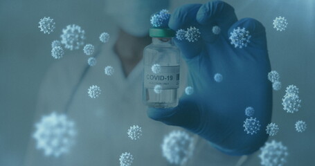 Image of covid 19 cells and masked gloved doctor holding vaccine