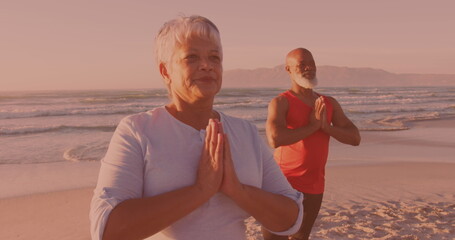 African american senior couple practicing yoga together at the beach
