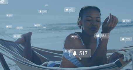 Image of social media reactions over happy african american woman in hammock on beach