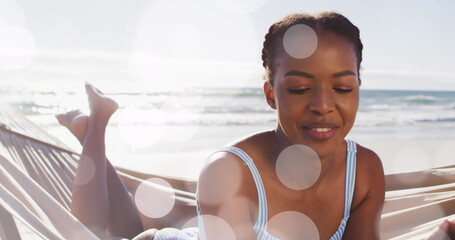 Image of dots over happy african american woman in hammock on beach