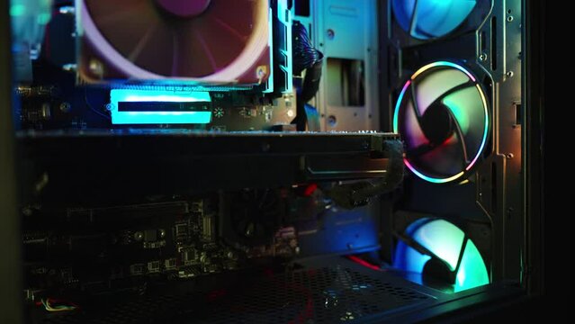 Inside a gaming PC, RGB lighting, numerous colorful fans, and electronic components in the dark.