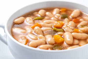 white beans soup with vegetables in white bowl isolated on white background. close up