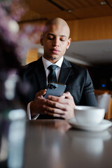 African american businessman in classic attire using smartphone near coffee in business center