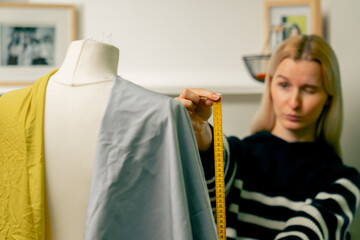 in a sewing workshop seamstress works with a mannequin on a blue fabric measures with a centimeter