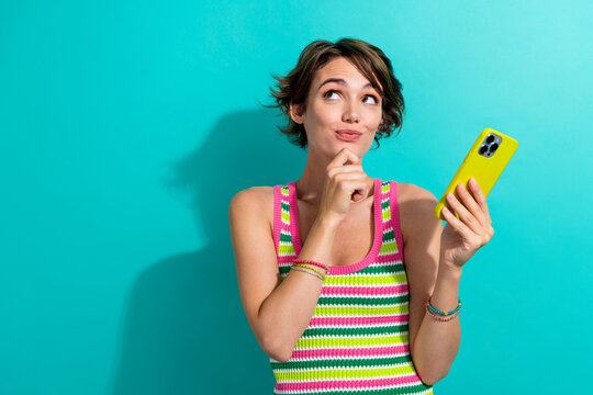 Portrait of minded cute girl hand touch chin hold smart phone look empty space isolated on turquoise color background