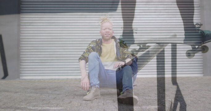 Image of man skateboarding over albino man sitting on skateboard