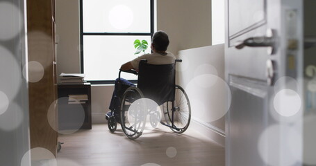 Image of light spots over senior biracial man sitting in wheelchair