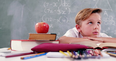 A pensive child sits at a desk with school supplies and an apple