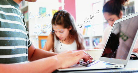 Image of mathematical equations floating over schoolchild using laptop computer with classmates in t