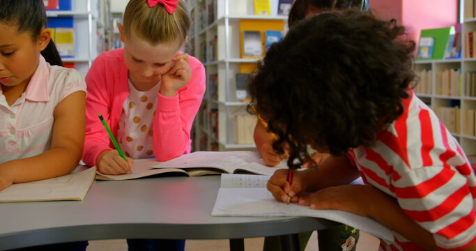 Three children are focused on writing in notebooks at a library