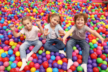 Happy little kids sitting on colorful balls in ball pit
