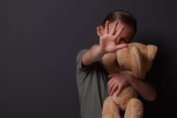 Child abuse. Girl with toy making stop gesture near grey wall, selective focus. Space for text